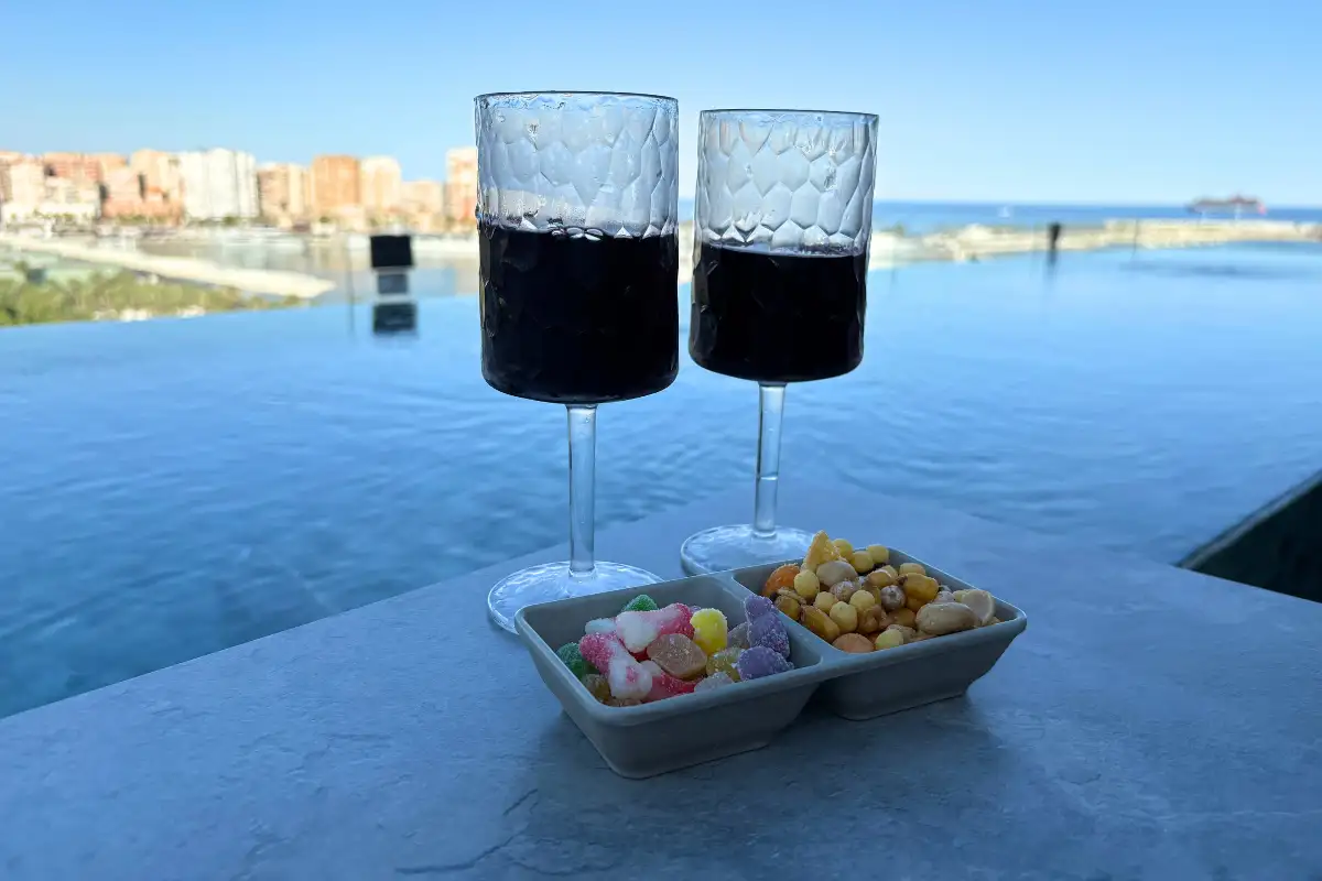 Two red cocktails and snacks at the pool edge with sea view at Lolita Skyview in Malaga