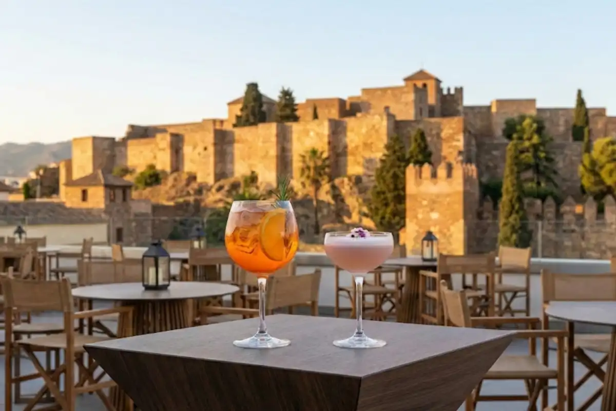 A bright orange spritz on a rooftop table with the Alcazaba fortress lit at golden hour behind it
