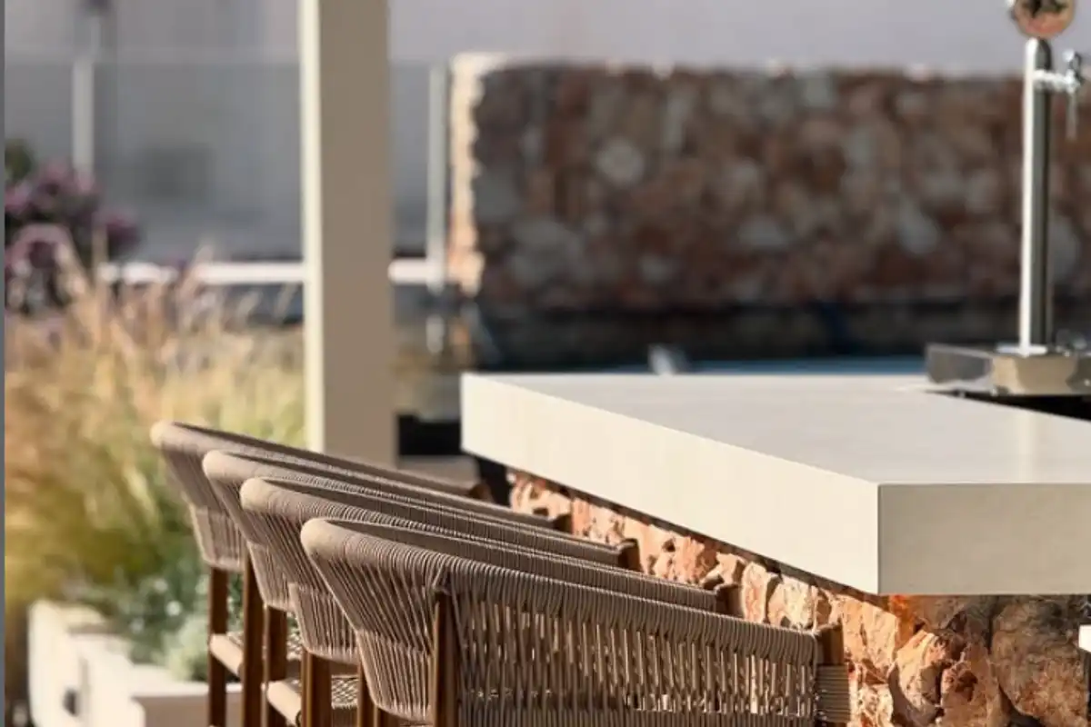 Woven bar stools beside a stone rooftop counter at Well and Come Malaga